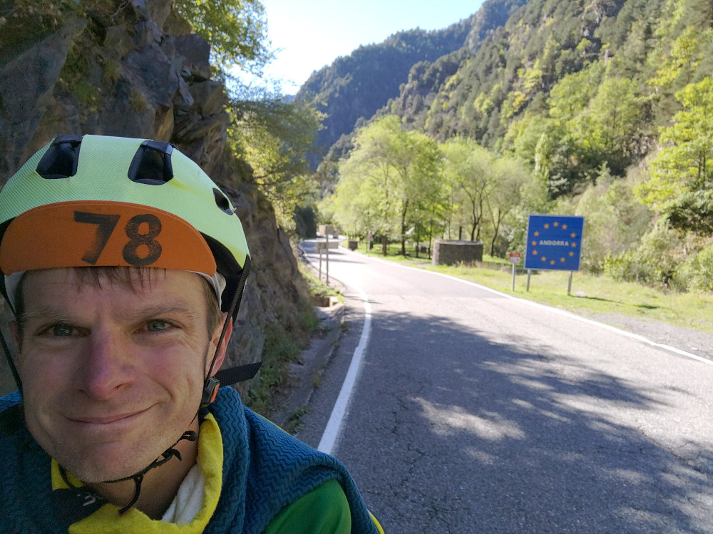 James smiling with steep valley and Andorra sign in the background.