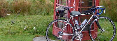 Bicycle leaning against an old phone box.