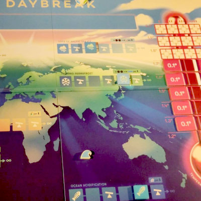 Board game laid out on wooden table. Cards and player board in the foreground, in the background is the main Daybreak board showing globe and thermometer.