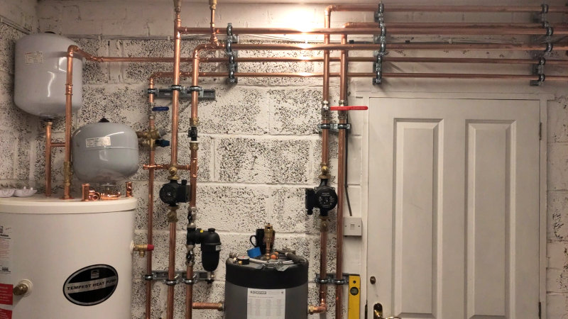 Copper pipes and water cyclinders attached to the wall inside a garage.