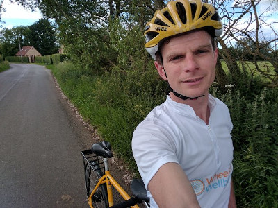 James in white Wheels for wellbeing jersey standing astride the yellow tandem.