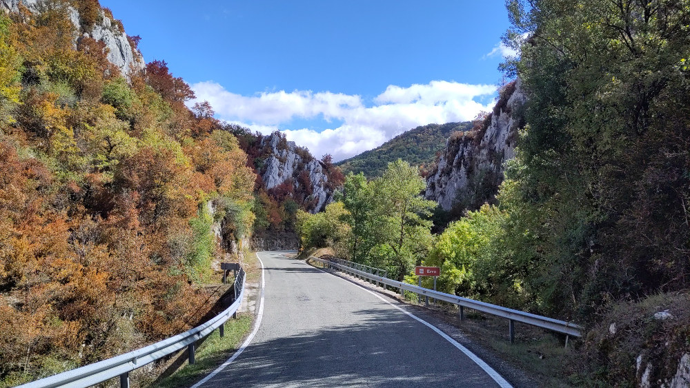 Road winding through small gorge with autumnal trees and blue sky